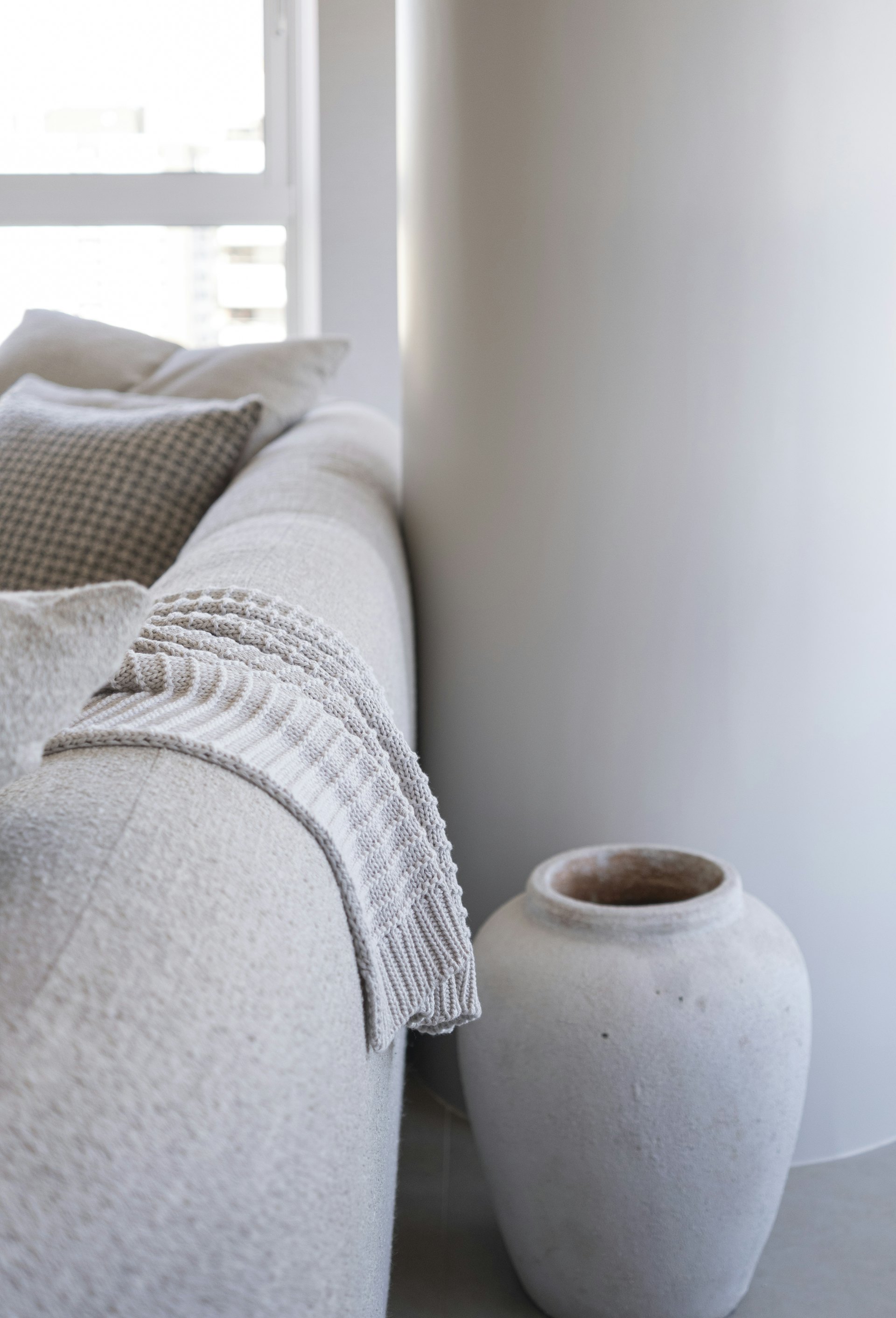 A soft throw draped over a neutral sofa beside a textured vase